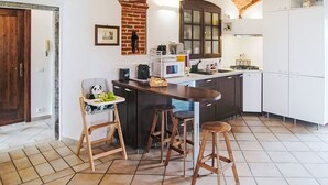 Una cocina con techo de ladrillo, armarios blancos, una isla central, taburetes y una trona para bebé.