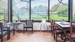 Un invernadero con vistas a un jardín, que incluye una mesa de comedor, sillas y una mesita con una maceta.