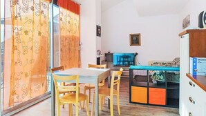 Un soggiorno con tavolo da pranzo, sedie, televisore, libreria e un'ampia finestra con tende.