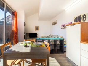 A compact living space with a dining table, chairs, a sofa, a television, and a microwave.
