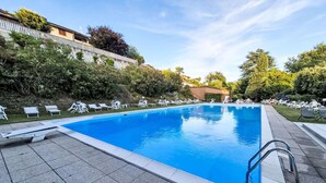 Una piscina rettangolare con bordo piastrellato, circondata da lettini e vegetazione.