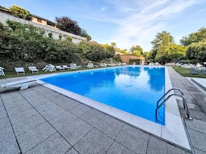 Ein rechteckiger Pool mit Fliesenränder, umgeben von Liegestühlen und viel Grün.