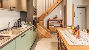 A modern kitchen with a wooden staircase, a dining area with a table set for two, and a small wooden shelf with kitchen items. - Stunning  villa for 4 people with WIFI, A/C, TV, patio and pets allowed (Verceia)