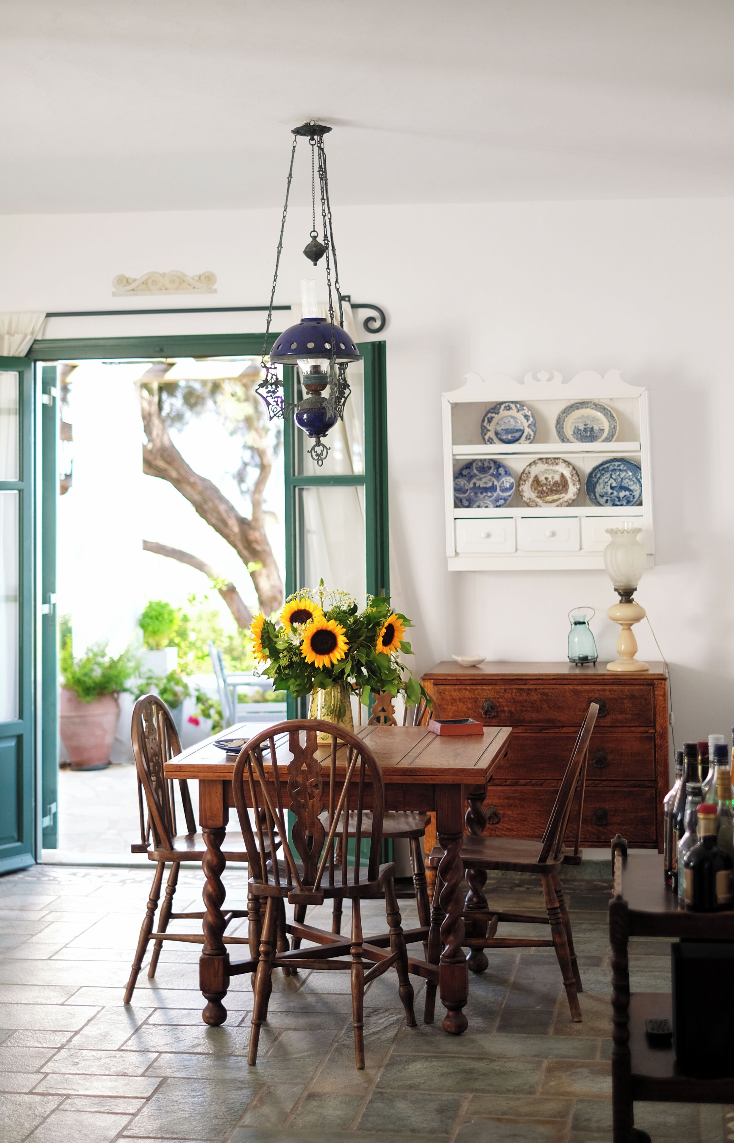 Een eethoek met een houten tafel, stoelen, een vaas met zonnebloemen, een hanglamp en een wandplank.