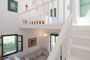 A multi-level interior with a staircase, a sofa, a window with curtains, and a wall-mounted picture. - Santa Maria Architect's Villa with Atrium & Gardens (Naousa)