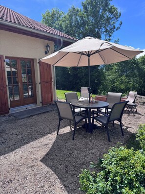 Eine Terrasse im Freien mit einem runden Tisch, vier Stühlen und einem großen Sonnenschirm.