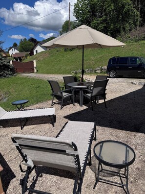 An outdoor patio with a table, chairs, a bench, and a large umbrella. - Your Alpine Retreat — Spa Treatments, Fine Dining, and Adventure (Saint-Martin-d'Uriage)