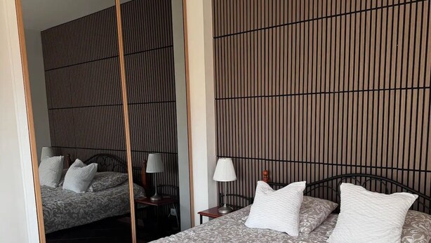 A bedroom with a bed, a mirror, a nightstand, and a wall with vertical lines. - Your Alpine Retreat — Spa Treatments, Fine Dining, and Adventure (Saint-Martin-d'Uriage)