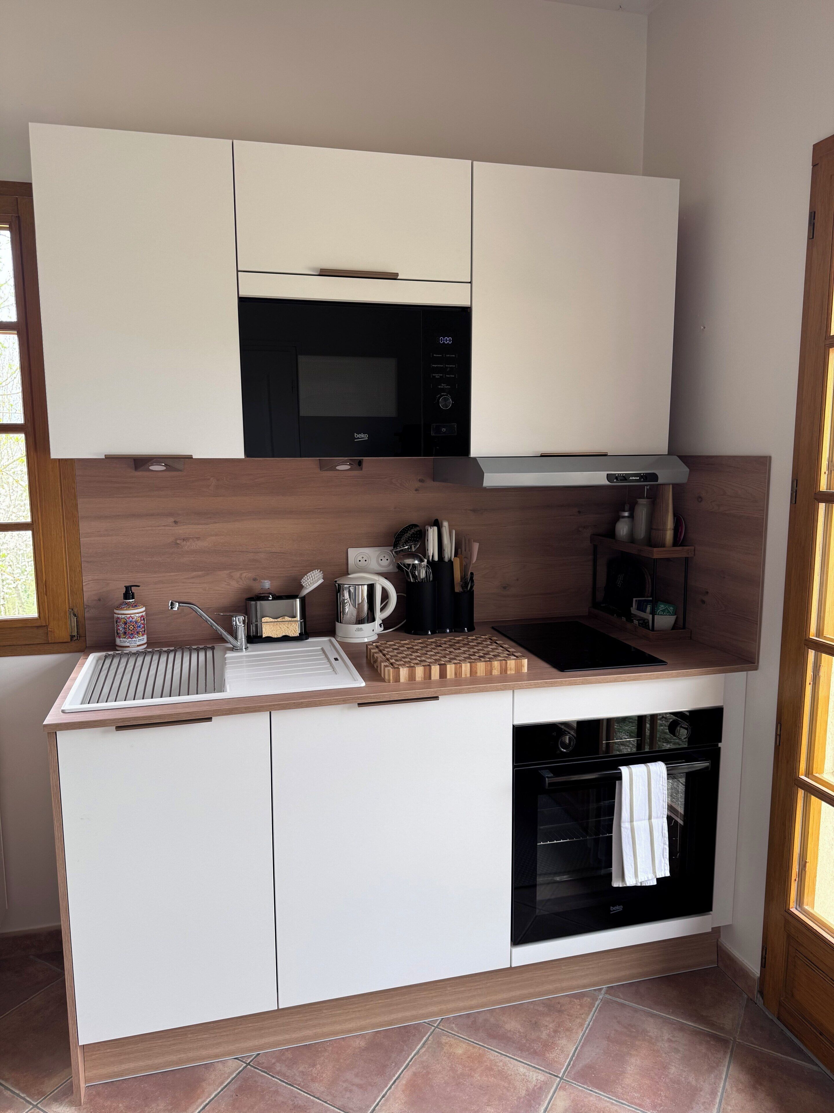 A compact kitchen with a microwave, sink, and oven, wooden cabinets, and a window.