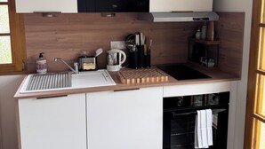 A compact kitchen with a microwave, sink, and oven, wooden cabinets, and a window. - Your Alpine Retreat — Spa Treatments, Fine Dining, and Adventure (Saint-Martin-d'Uriage)