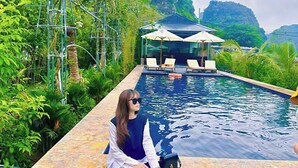 A person sitting by a pool with a view of a mountain and a building in the background. - Hang Mua Peaceful Retreat (Hoa Lu)