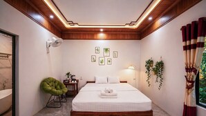 A bedroom with a bed, bedside table, lamp, green chair, and a window with curtains. - Hang Mua Peaceful Retreat (Hoa Lu)
