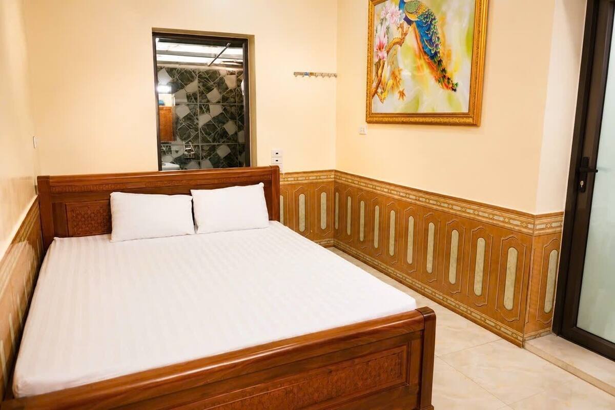 A bed with a wooden headboard, a window with a geometric pattern, and a framed painting on the wall.