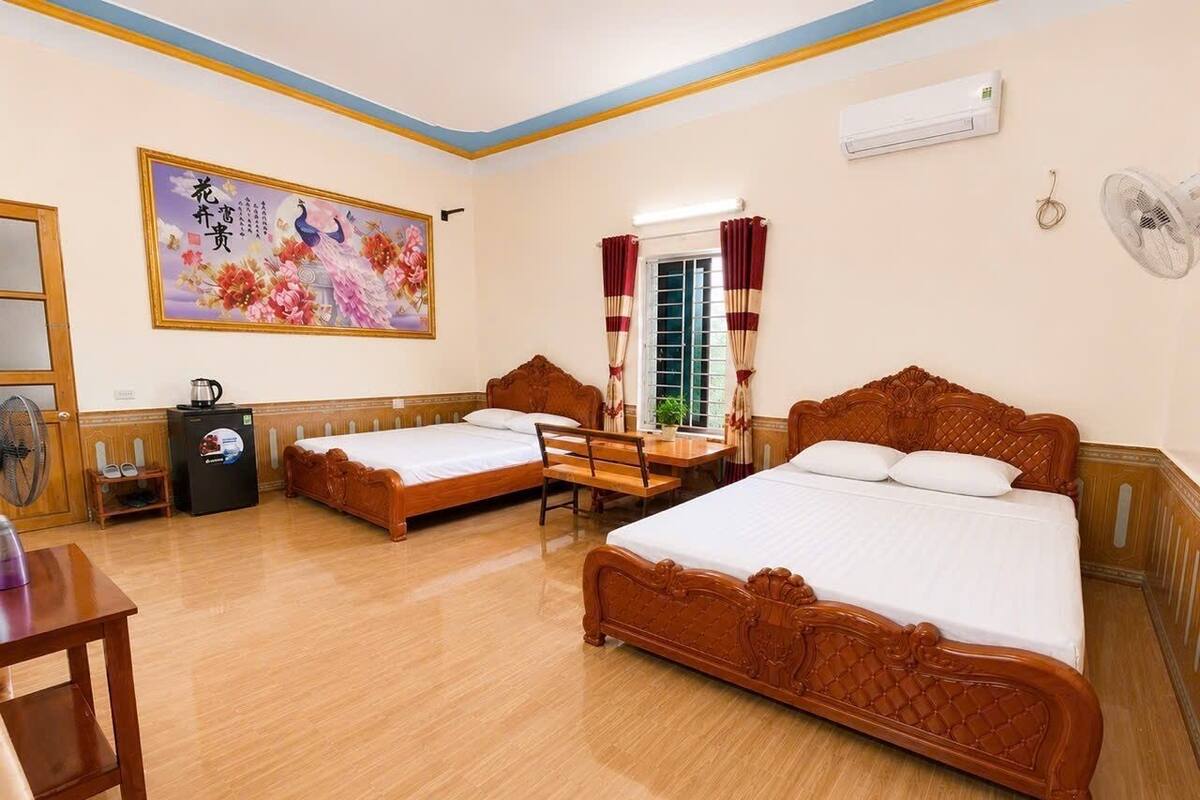 A hotel room with two single beds, a wooden desk, a chair, a radiator, and a wall-mounted air conditioner.