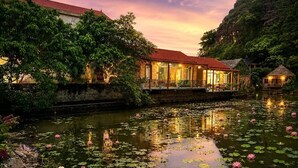 A riverside building with a red roof, surrounded by water lilies and greenery. - Hang Mua Peaceful Retreat (Hoa Lu)