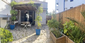 Ein Innenhof mit Steinboden, einer Holz-Pergola, Topfpflanzen und einem Tisch mit Stühlen.