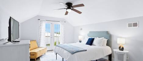 Un dormitorio con cama, ventilador de techo, escritorio con televisor y ventana con cortinas.