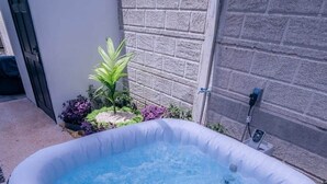 Uma banheira de hidromassagem inflável em um quintal com muro de tijolos e plantas.