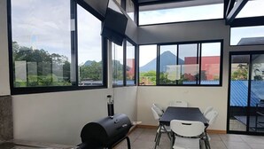 Eine Terrasse mit Grill, Tisch und Stühlen sowie große Fenster mit Blick auf einen Berg.