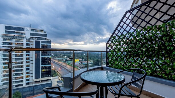 A balcony with a glass table and chairs, a view of a cityscape, and a green plant wall. - Nova 2-bedroom apartment in Nairobi (Nairobi)