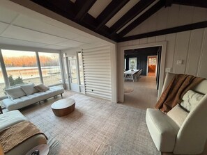 A spacious living area with a sofa, a round coffee table, and a view of a lake through large windows. - Le Petit Manitou | Where Montréal disappears and nature takes over (Laval)