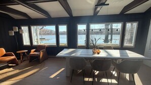 Ein Essbereich mit einem großen Tisch und Stühlen, einem Teppich und Blick auf einen See durch große Fenster.