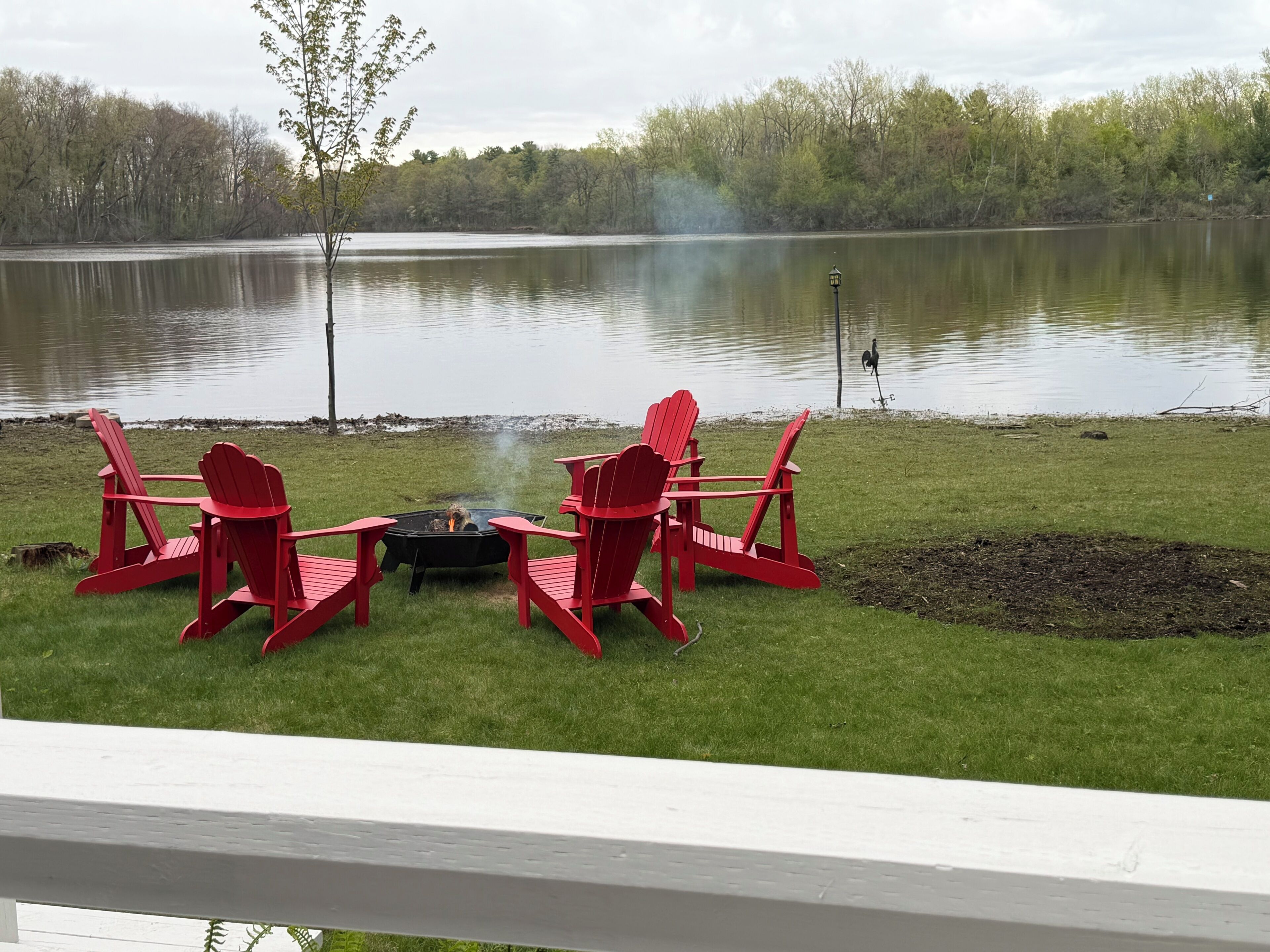 A lakeside deck with red Adirondack chairs, a fire pit, and a view of the lake.