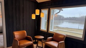 Ein Zimmer mit zwei Ledersesseln, einem kleinen runden Tisch und Seeblick durch große Fenster.