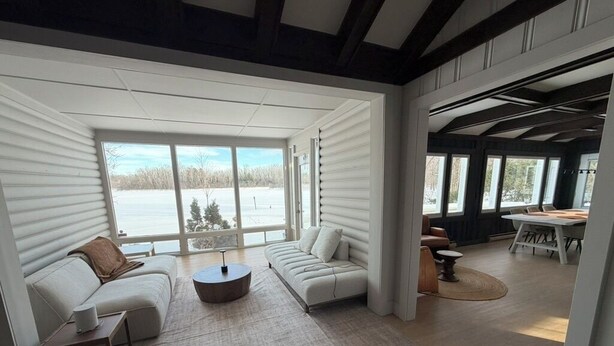 Ein modernes Interieur mit einer Couch, einem Couchtisch und einem Essbereich, große Fenster mit Blick auf eine verschneite Landschaft.