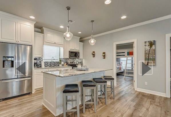 A modern kitchen with white cabinetry, stainless steel appliances, a central island with bar stools, and pendant lighting. - 3-bedroom/2 bath house in the beautiful Sandy Shores neighborhood. (Bolivar Peninsula)
