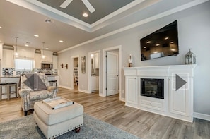 A spacious living room with a fireplace, a television mounted above it, and a kitchen in the background. - 3-bedroom/2 bath house in the beautiful Sandy Shores neighborhood. (Bolivar Peninsula)