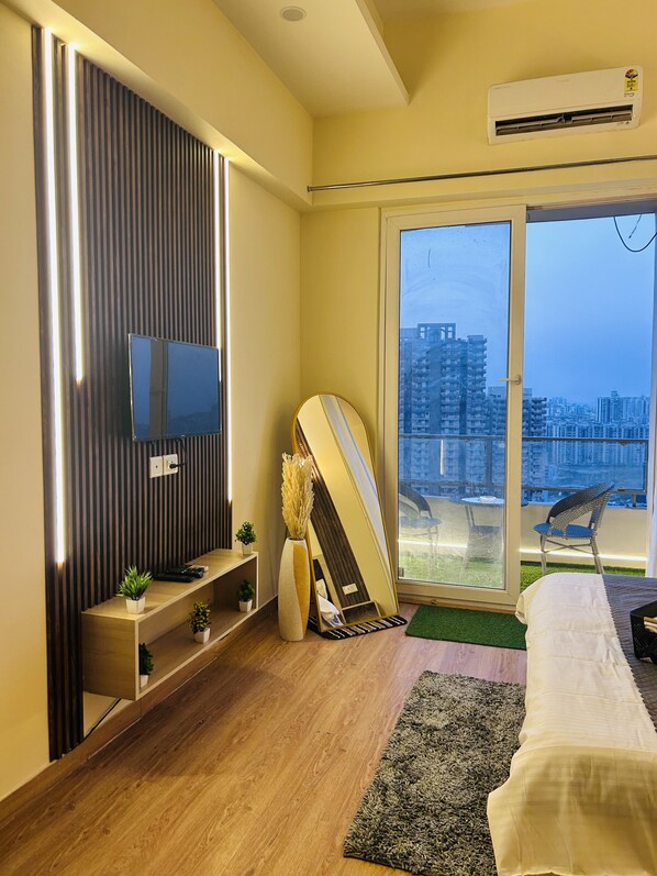 A modern bedroom with a TV, a surfboard, and a city view.