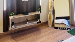 A modern room with a flat-screen TV mounted on a wooden panel wall, a console table with plants, a large mirror, and a wooden floor.