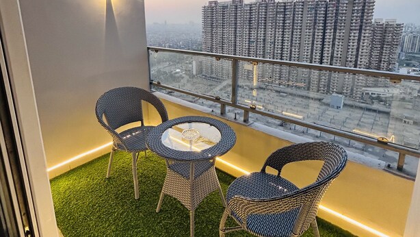 A balcony with two wicker chairs and a small table, overlooking a cityscape with high-rise buildings.