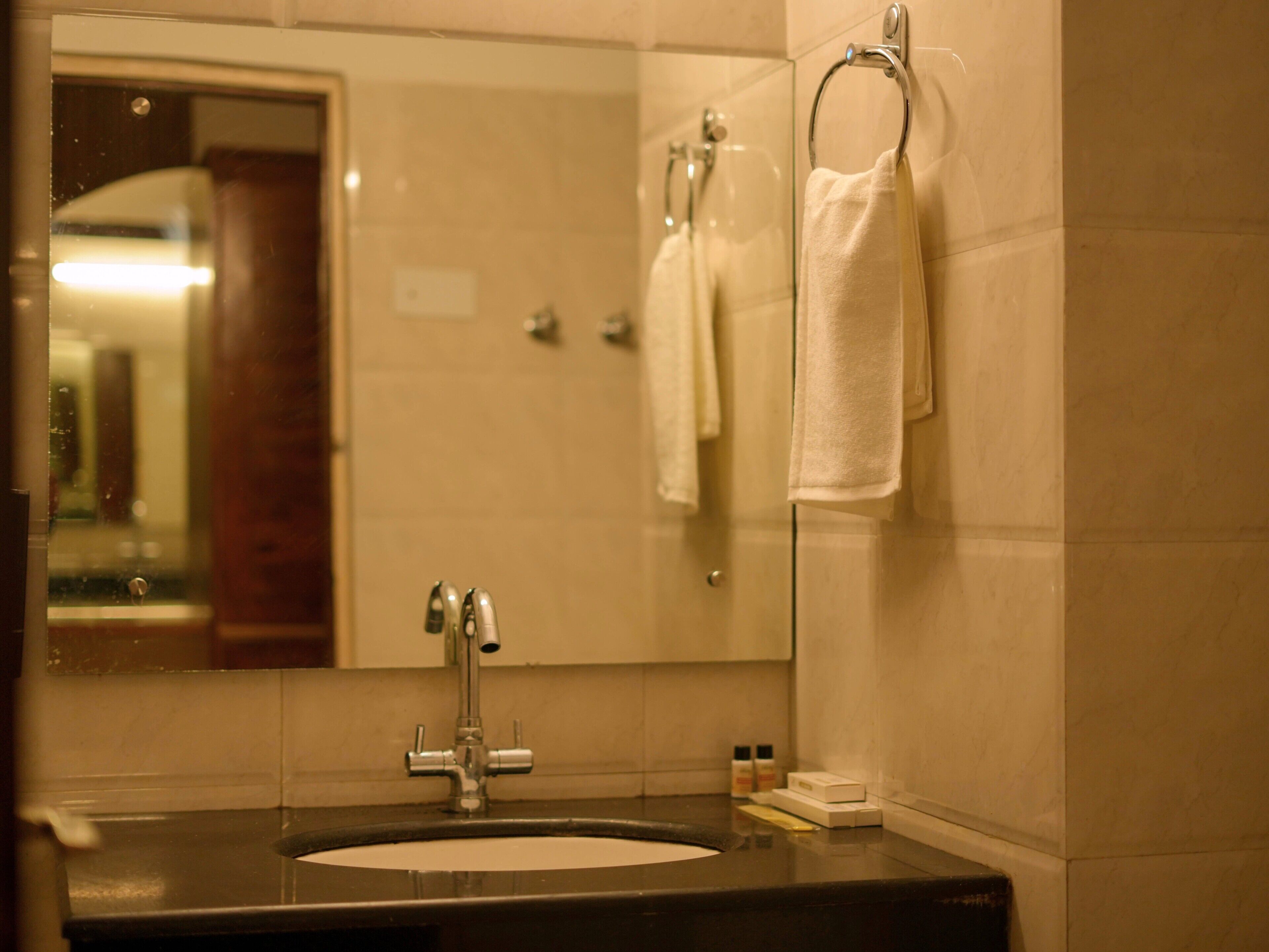 A bathroom with a sink, mirror, towel rack, and toiletries.