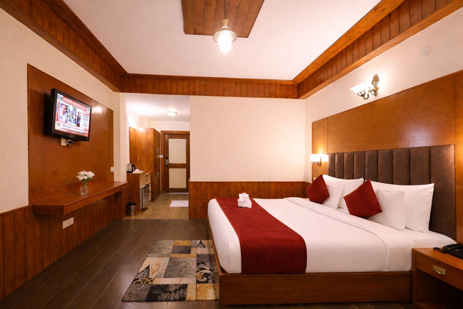 Een hotelkamer met een groot bed, houten lambrisering, een televisie en een klein bureau met een bloevas.