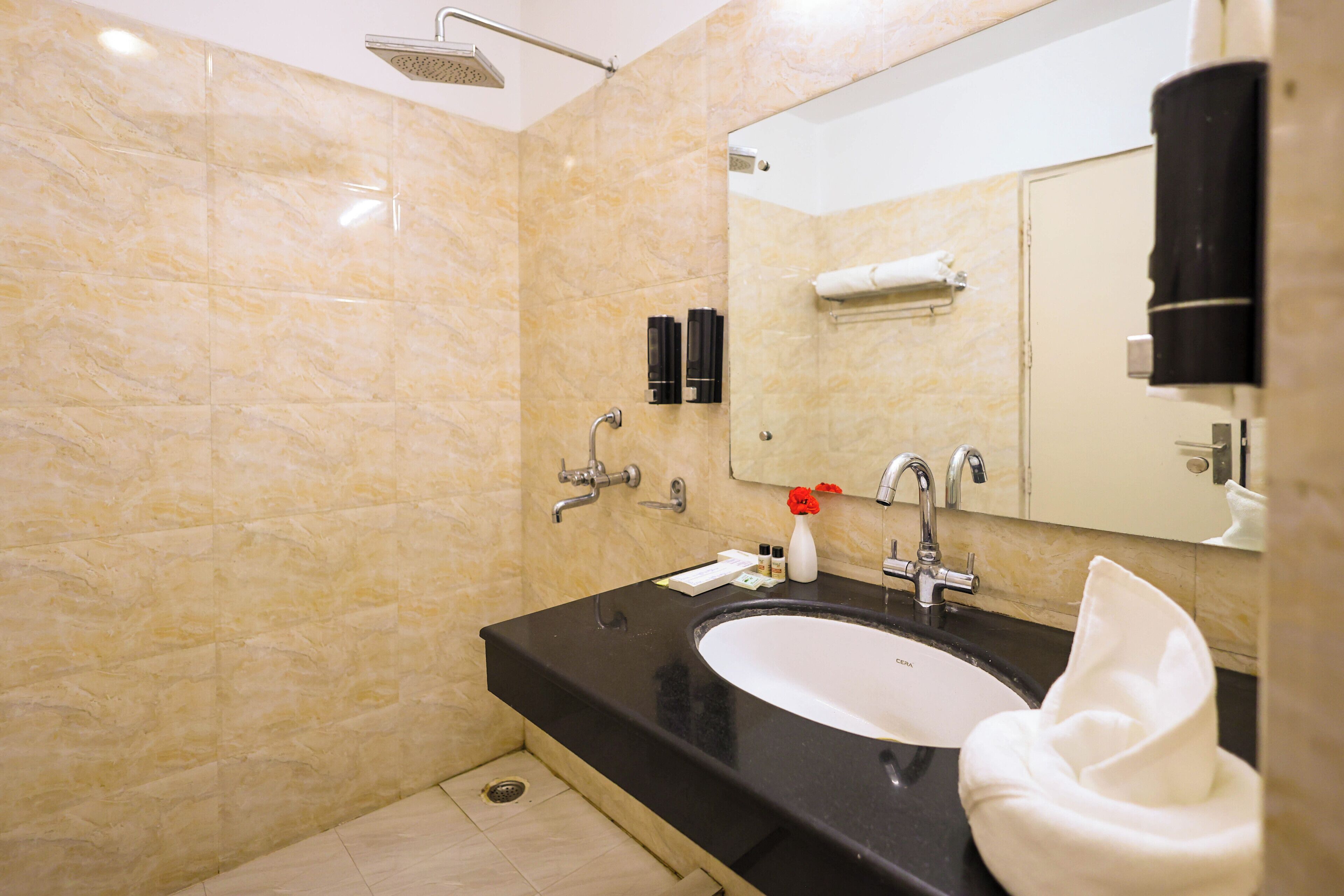 Casa de banho com lavatório, espelho, chuveiro e porta-toalhas.