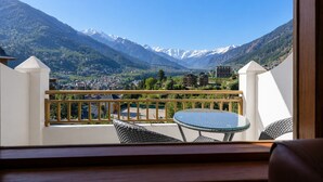 Varanda com mesa e cadeiras, com vista para uma paisagem montanhosa e edifícios.