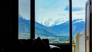 Quarto com uma grande janela que oferece vista para montanhas nevadas e um vale abaixo.