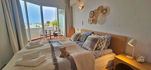 A hotel room with a bed, a small table, a chair, a wall-mounted lamp, and a view of the outside. - Charming flat with cozy terraces just a stone's throw from the beach (Calahonda)