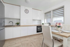 A modern kitchen with white cabinets, a wooden countertop, a built-in oven, and a dining area with a table set for two.