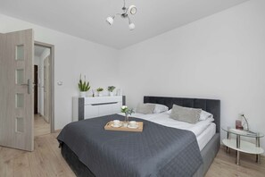 A modern bedroom with a large bed, bedside tables, a wardrobe, and a door leading to another room.