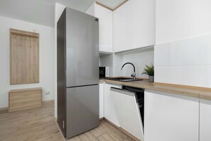 A modern kitchen with a stainless steel refrigerator, white cabinets, a wooden countertop, and a dishwasher.