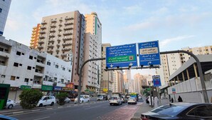 Een drukke stadstraat met meerlaags gebouwen, verkeersborden en verschillende voertuigen.