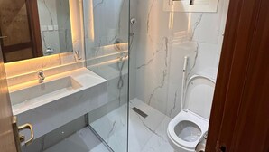 Een moderne badkamer met een douche met glazen wand, een grote spiegel en een toilet.
