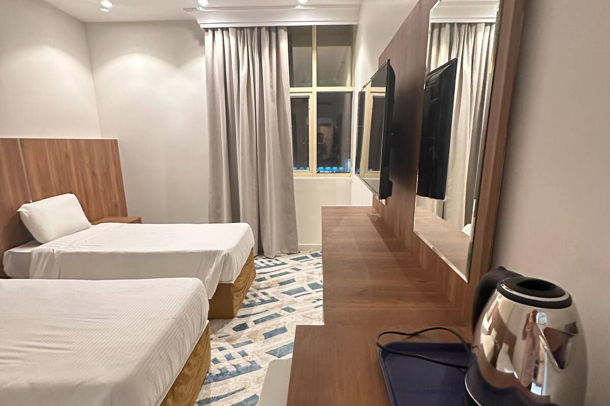 A hotel room with two beds, a large mirror, a coffee maker, and a view of the hallway.