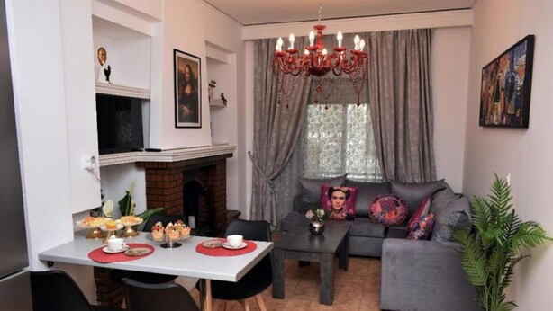 A living room with a sofa, a dining table with chairs, a fireplace, and a chandelier. - Art House by Helen in Soroni Rhodes (Rhodes)