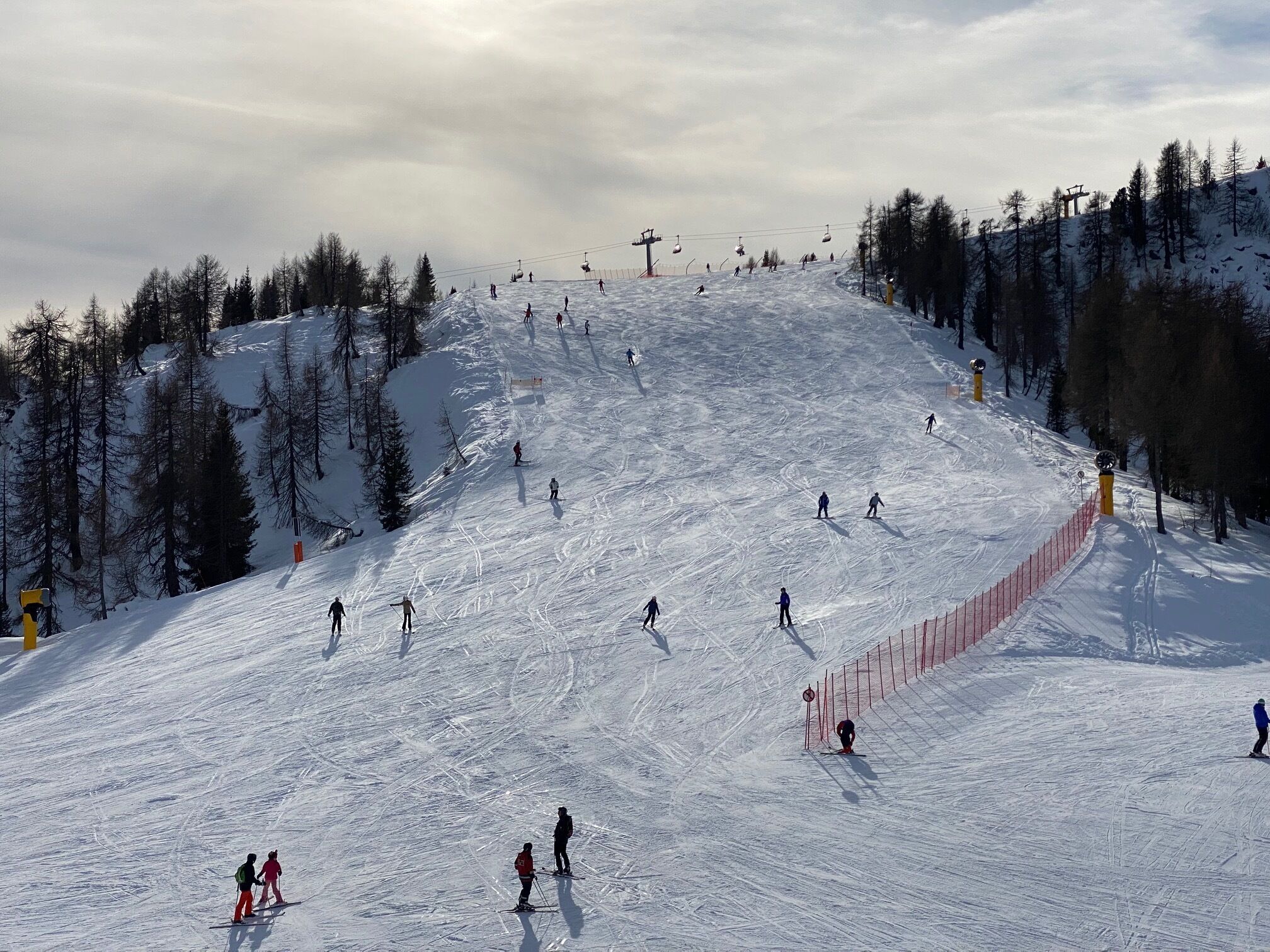 Une piste de ski avec des skieurs, un télésiège et une montagne boisée en arrière-plan.