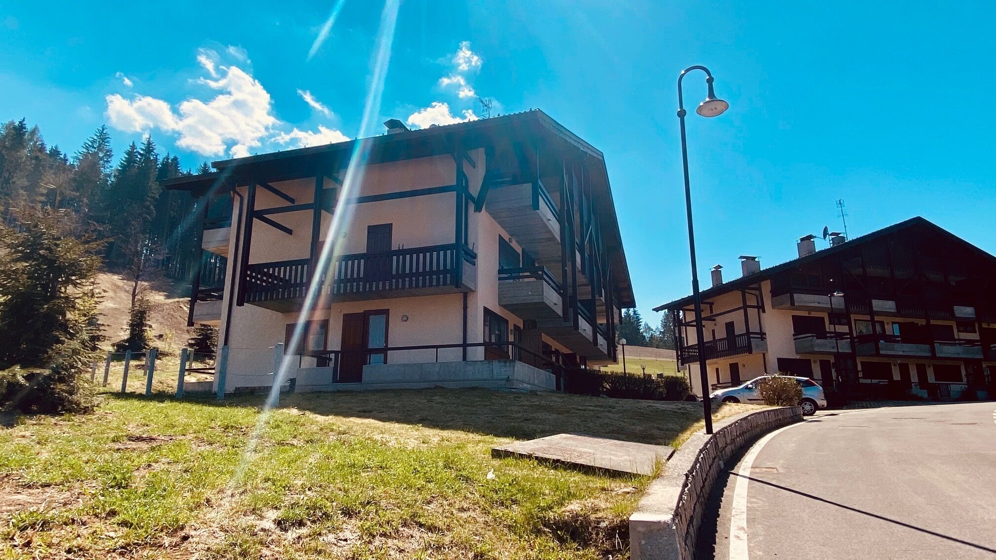 Un edificio de varios pisos con balcones, un área pavimentada en frente y una farola.