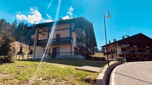 Un edificio de varios pisos con balcones, un área pavimentada en frente y una farola.